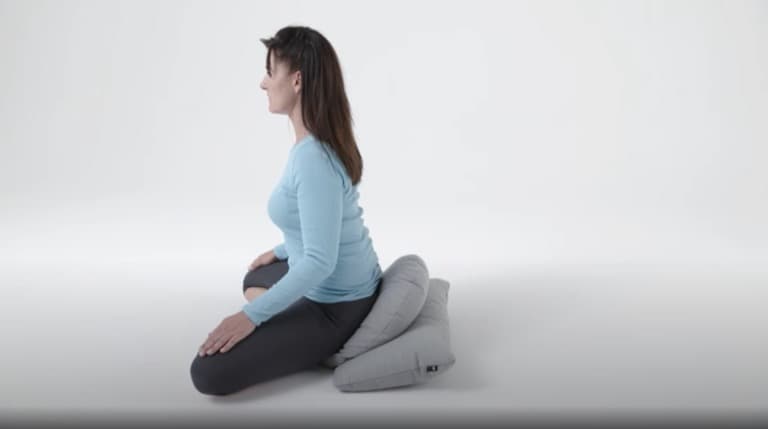 Woman sitting in a cross-legged position on the meditation cushion.